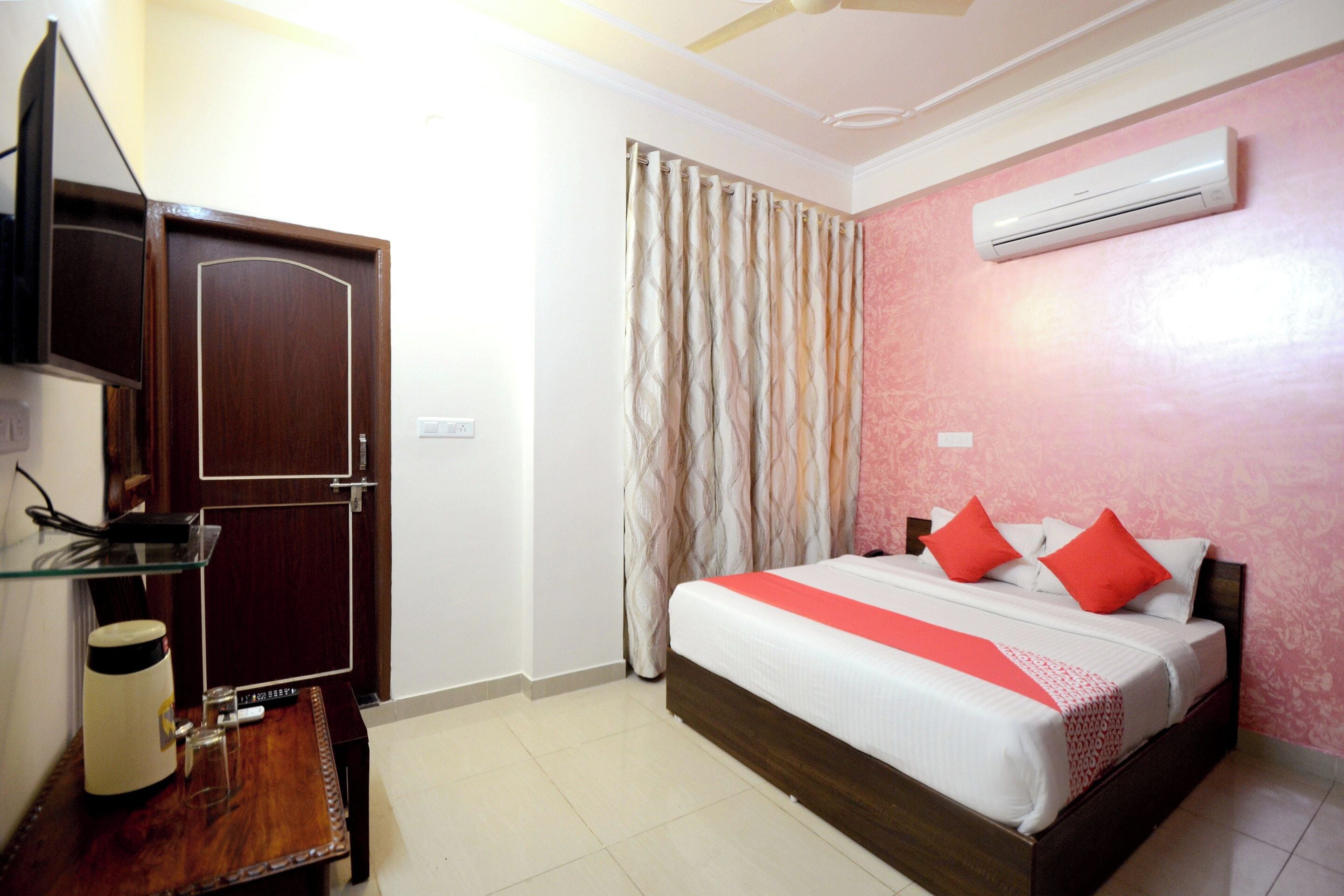 A hotel room with a bed, a television, a desk, and an air conditioning unit.