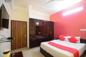 Una camera d'albergo con un letto, un armadio, una televisione e una parete decorata in rosso.