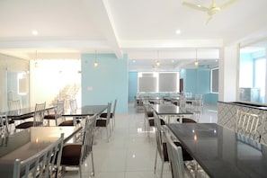 Un'ampia sala da pranzo con diversi tavoli e sedie, una ventola a soffitto e una scala sullo sfondo.