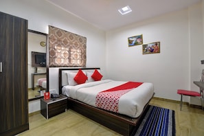 Una camera d'albergo con un letto, un comodino con il telefono, uno specchio e una parete con due quadri.