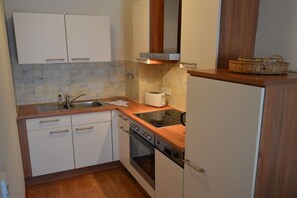 A compact kitchen with white cabinets, a built-in oven, a stovetop, and a microwave. - Holiday apartment Strandschlösschen 319607 (Kühlungsborn)