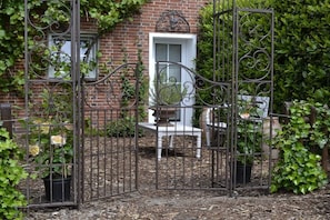 A gated garden area with a brick building, a white door, and a bench. - Holiday home with 2 bedrooms (Papenburg)