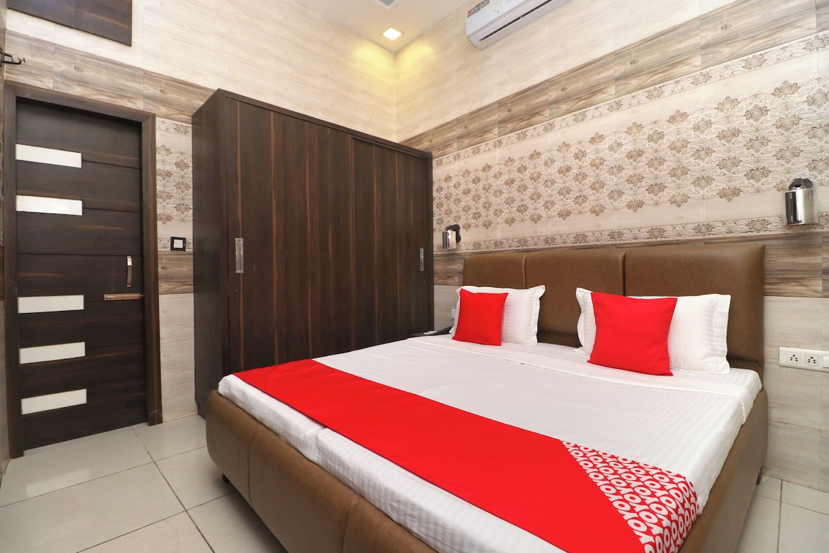 A hotel room with a large bed, a wardrobe, a patterned wall, and a ceiling light.
