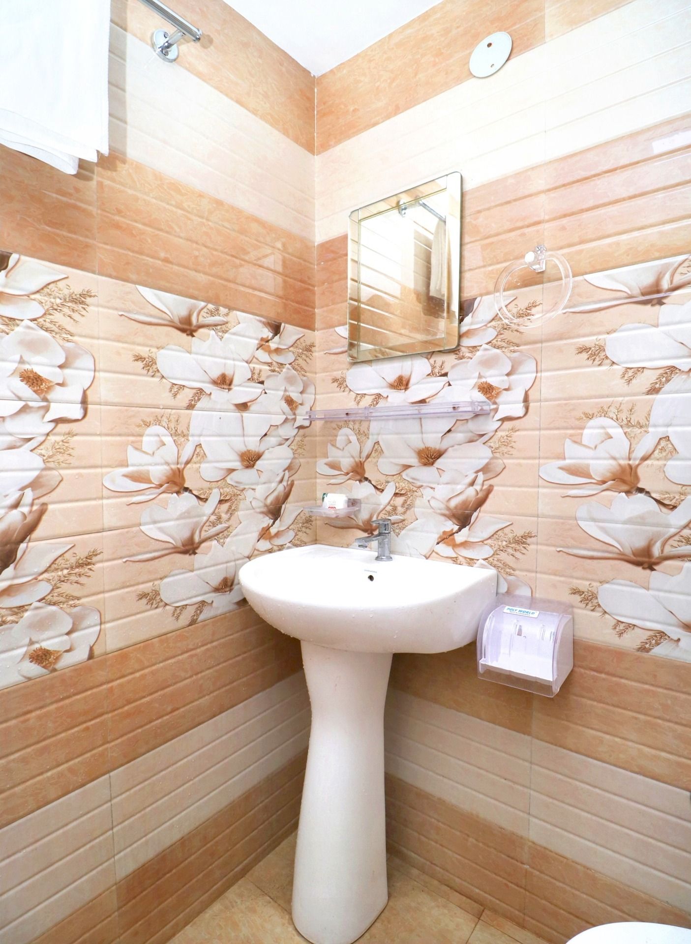 A bathroom with a white pedestal sink, a mirror, and a toilet. The walls are tiled with a floral pattern.