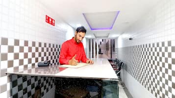 Una persona sentada a una mesa en un pasillo con paredes a cuadros, un techo con una lámpara y un letrero rojo en la pared.