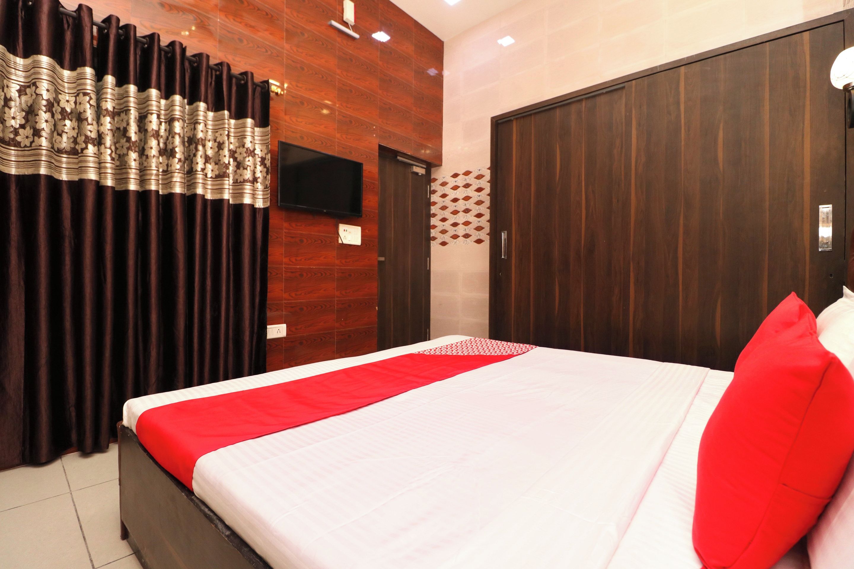 A hotel room with a bed, curtains, a television, and a wooden wall.