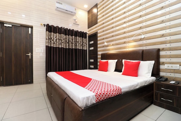 A hotel room with a large bed, a wooden headboard, a nightstand with a phone, and a wall-mounted air conditioning unit. - Hotel O Max (Jalandhar)