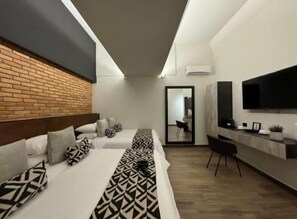 Una habitación de hotel moderna con pared de ladrillo decorativa, una cama grande con ropa de cama estampada, un televisor de pantalla plana, un escritorio y un espejo.