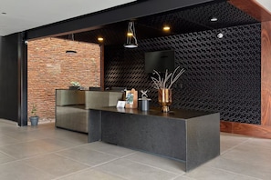 A reception area with a brick wall, a black textured wall, a reception desk, and a flat-screen TV. - Esplendor by Wyndham San Luis Potosi Monarca (San Luis Potosi)