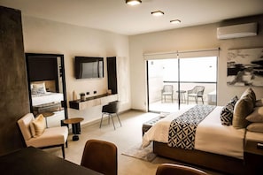 A modern hotel room with a bed, seating area, TV, and a balcony with chairs. - Esplendor by Wyndham San Luis Potosi Monarca (San Luis Potosi)