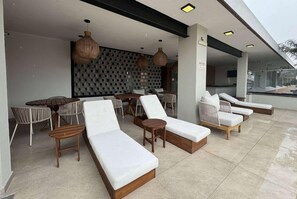 A modern outdoor lounge area with cushioned seating, a patterned wall, and hanging lights. - Esplendor by Wyndham San Luis Potosi Monarca (San Luis Potosi)
