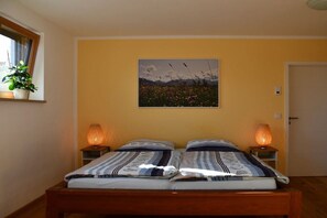 A room with a bed, two bedside lamps, a window with a plant, and a wall-mounted picture. - New 2-room holiday apartment in Murnauer Moos (Schwaigen)
