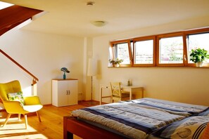 A bedroom with a bed, a desk, a chair, a cabinet, and a window with plants. - New 2-room holiday apartment in Murnauer Moos (Schwaigen)
