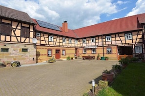 A courtyard with traditional half-timbered buildings, a paved area, and potted plants. - Holiday apartment with 1 bedroom (Uhlstädt-Kirchhasel)