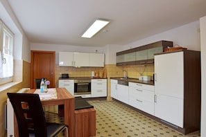 A compact kitchen with white cabinets, a wooden dining table, and a tiled floor. - Holiday apartment with 1 bedroom (Uhlstädt-Kirchhasel)