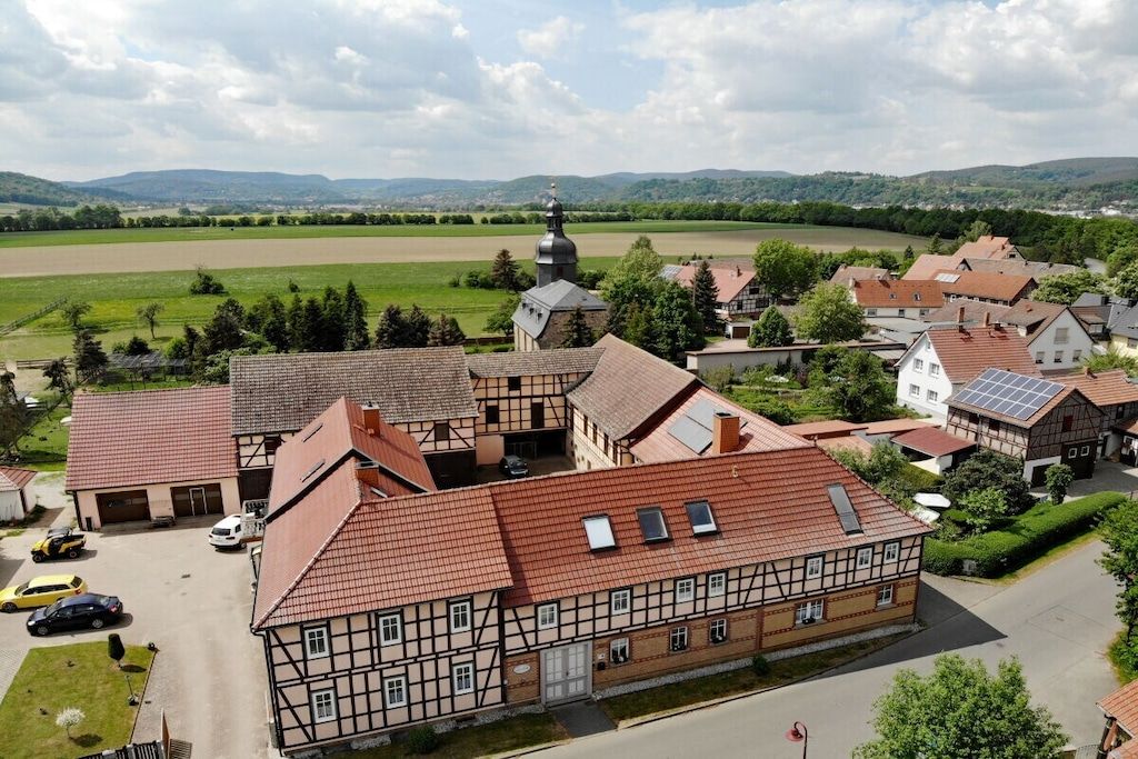 A traditional half-timbered building with a red-tiled roof, surrounded by other residential structures and a church with a dome.
