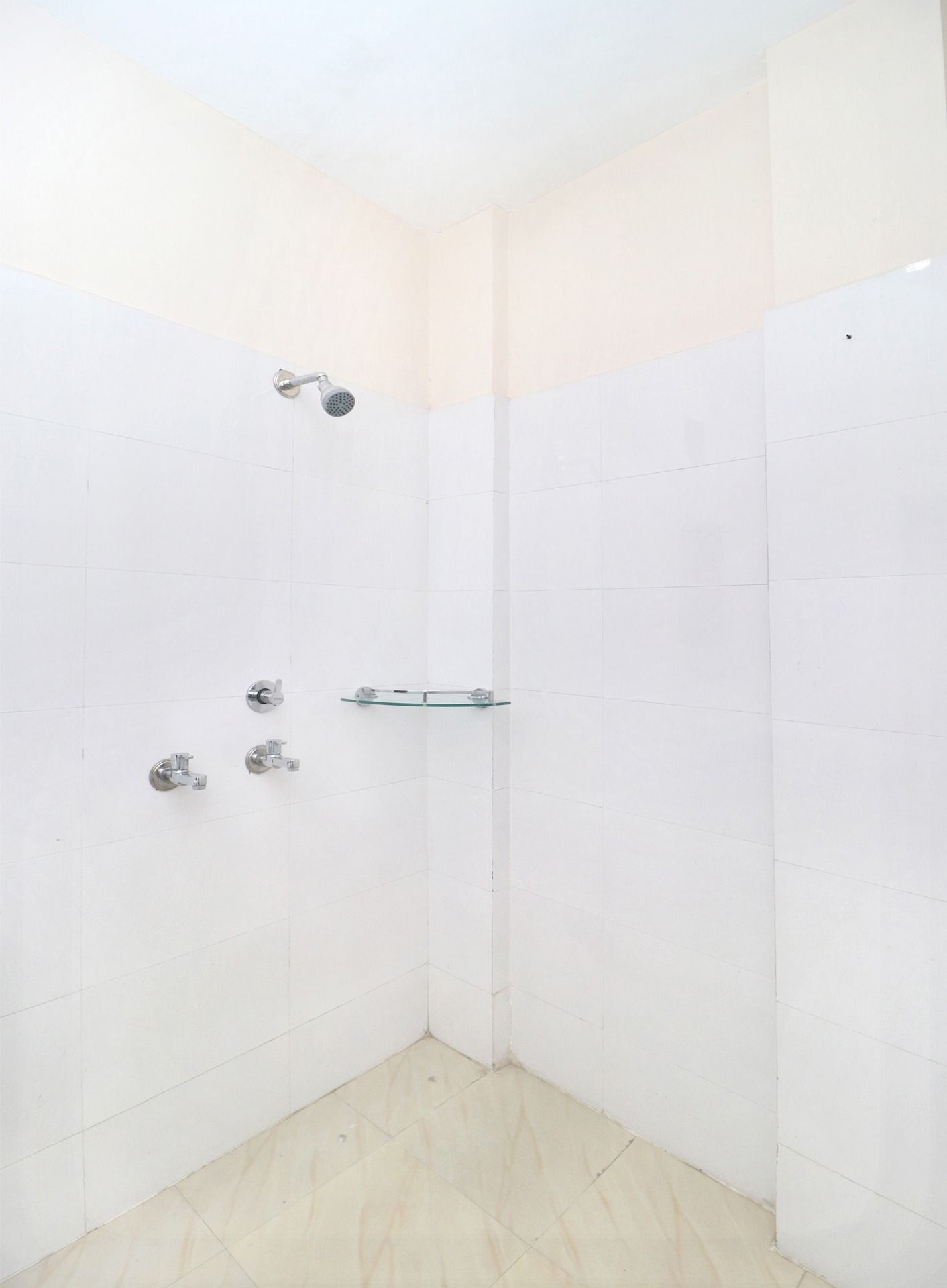 A small, white-tiled shower stall with a glass shelf and a handheld showerhead.