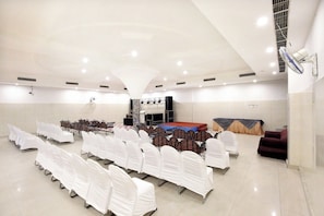 Un salón amplio con filas de sillas blancas, un escenario con plataforma roja y un ventilador de techo.