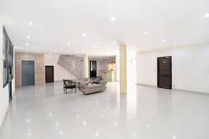 Un hall d’entrée spacieux avec un escalier, un comptoir d’accueil et un espace détente comprenant un canapé et des fauteuils.