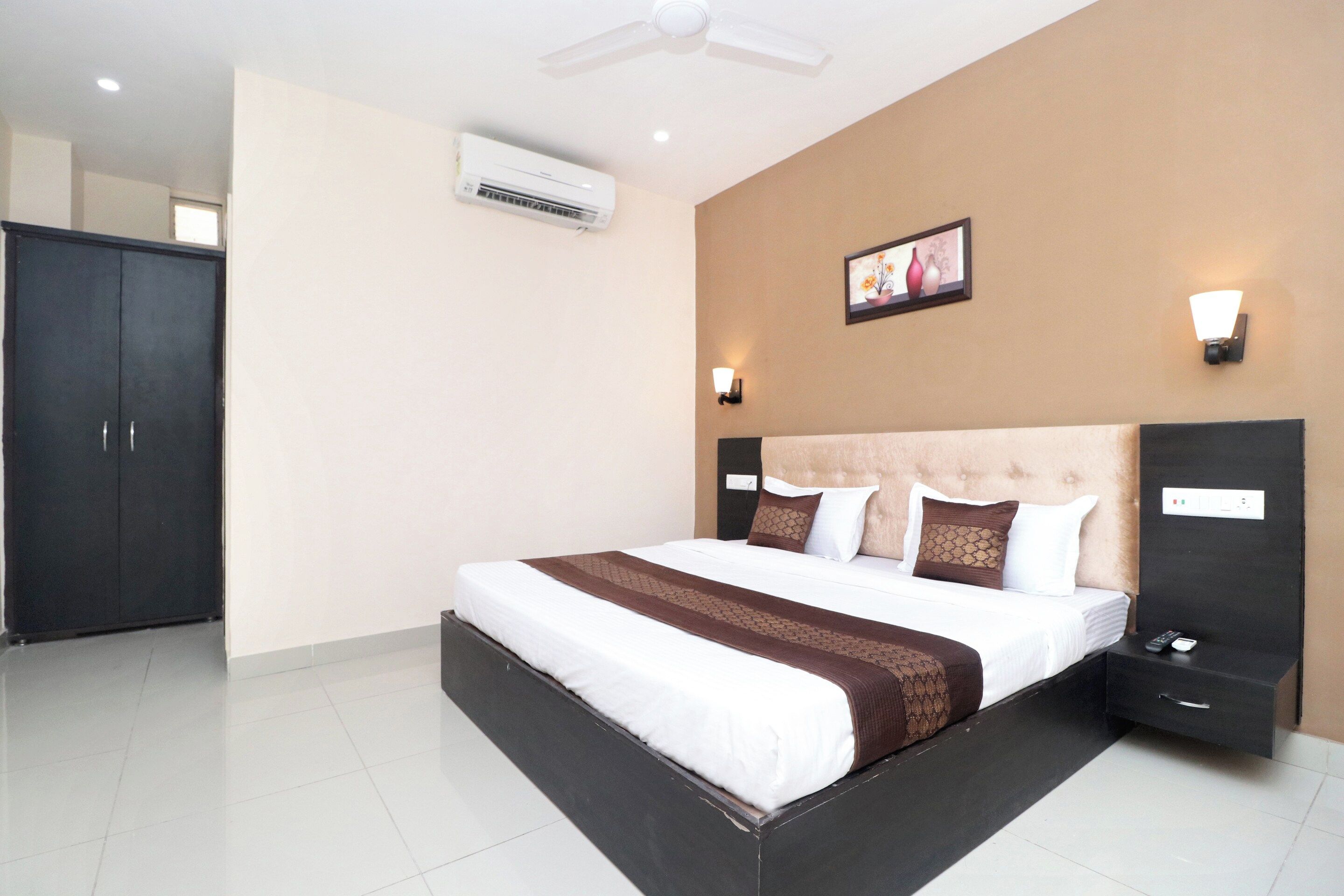Habitación de hotel con cama, mesitas de noche, equipo de aire acondicionado, ventilador de techo y un cuadro colgado en la pared.