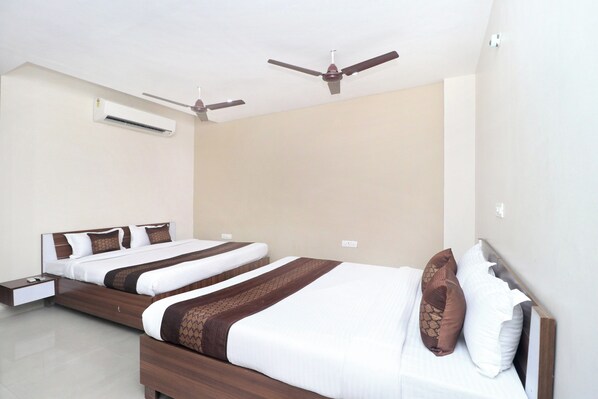 A hotel room with two beds, a ceiling fan, an air conditioning unit, and a bedside table.