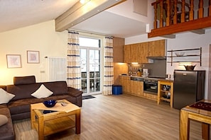A living room with a sofa, a coffee table, and a kitchen area with wooden cabinets, a stove, and a refrigerator. - Holiday apartment with 1 bedroom (Bodenmais)