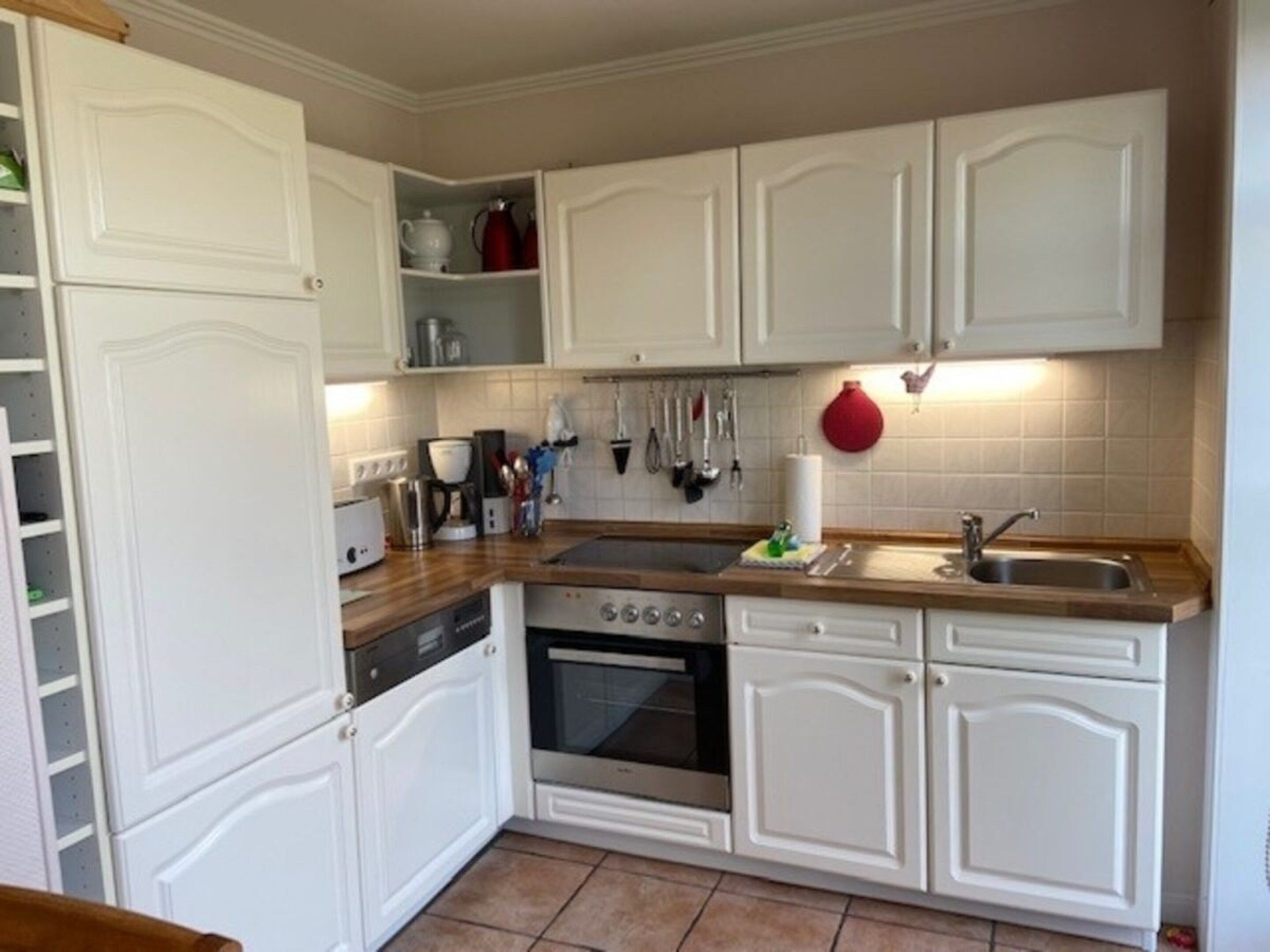 A kitchen with white cabinetry, a stove, a sink, and various kitchen utensils.