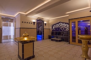Un vestíbulo amplio con diseño moderno, que cuenta con una zona de estar central, una pared decorativa con motivo de estrellas y una gran fuente dorada.