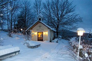 Una iglesia cubierta de nieve con una cruz en la fachada, una entrada iluminada y un sendero nevado que la lleva a ella.