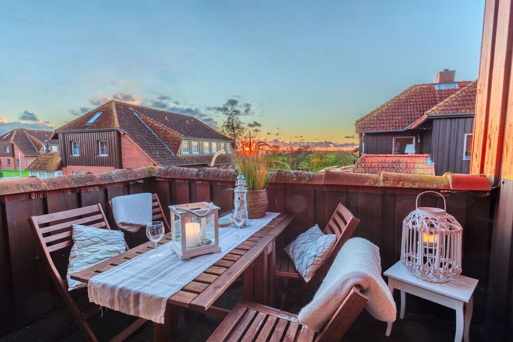 A wooden deck with a table set for dining, surrounded by chairs, and a lantern on a small table.