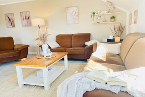 A living room with a brown sofa, a white coffee table, and a bookshelf with decorative items. - Holiday apartment with 1 bedroom (Fehmarn)