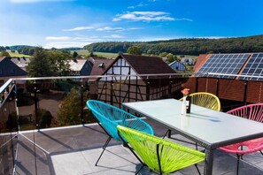 A balcony with a table and chairs, overlooking a village with traditional houses and solar panels. - Holiday apartment with 1 bedroom (Homberg\/Efze)