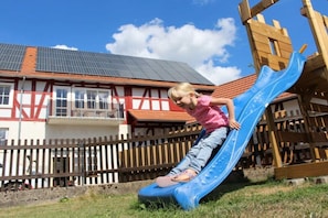 A child on a blue slide in front of a building with a red and white facade. - Holiday apartment with 1 bedroom (Homberg\/Efze)
