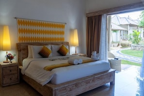 A hotel room with a wooden bed, two bedside lamps, a patterned curtain, and a view of the outdoor area. - 69 Resort Nusa Penida by Loccal Collection (Penida Island)