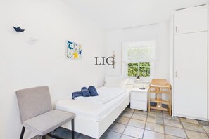 Ein heller Raum mit einem Bett, einem Sessel, einem Schreibtisch und einem Kleiderschrank.