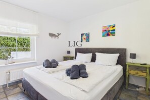 A hotel room with a large bed, two bedside tables, a window with blinds, and artwork on the walls. - Holiday apartment Seal Bank (Langeoog)