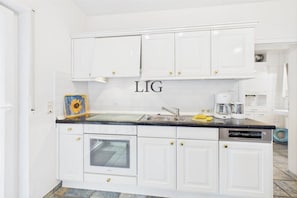 A kitchen with white cabinets, a dishwasher, and a coffee maker. - Holiday apartment Seal Bank (Langeoog)