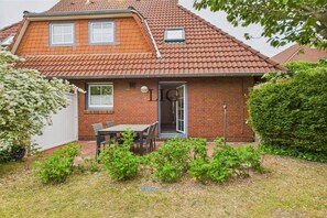 A two-story house with a red-tiled roof, a brick exterior, and a small patio with a table and chairs. - Holiday apartment Seal Bank (Langeoog)