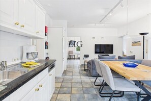 A modern kitchen with white cabinets, a granite countertop, and a dining area with a wooden table and chairs. - Holiday apartment Seal Bank (Langeoog)