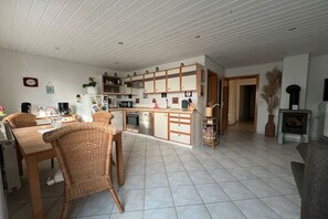 Een moderne keuken met witte kasten, een zithoek met rieten stoelen en een open haard.