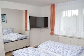 A bedroom with a bed, a television mounted on the wall, and a window with curtains. - Holiday apartment with 2 bedrooms (Kurort Oberwiesenthal)