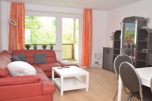 A living room with a red sofa, a white coffee table, and a dining area with a table and chairs. - Holiday apartment with 2 bedrooms (Kurort Oberwiesenthal)