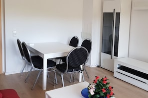 Un comedor con una mesa y sillas blancas, un pequeño sofá rojo y un armario blanco.