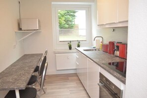 A compact kitchen with a dining table, a built-in oven, and a window with blinds. - Holiday apartment with 2 bedrooms (Kurort Oberwiesenthal)