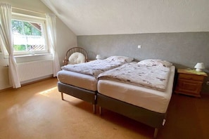 A bedroom with two beds, a window with curtains, a radiator, and a nightstand with a lamp. - Holiday apartment in Monschau-Höfen with Wi-Fi (Monschau-Höfen)