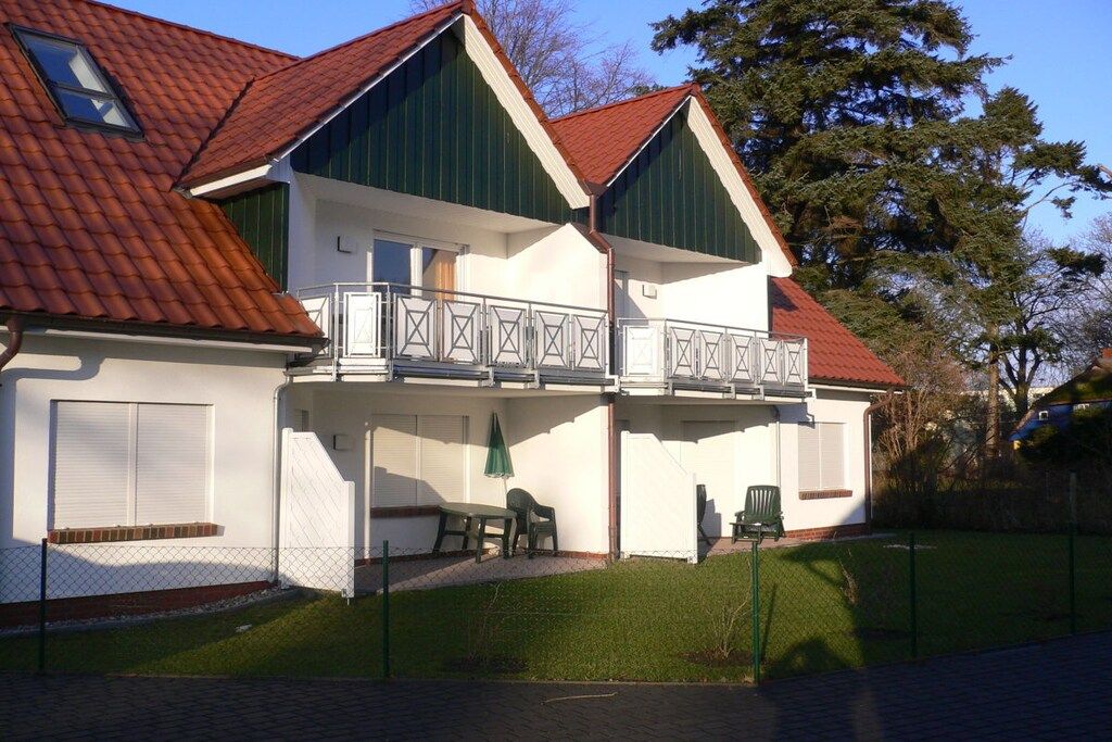 A two-story house with a balcony, a fenced yard, and a green lawn.