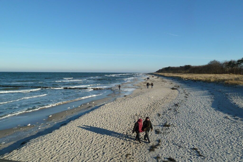 A sandy beach with people walking, a clear sky, and the ocean in the background.
