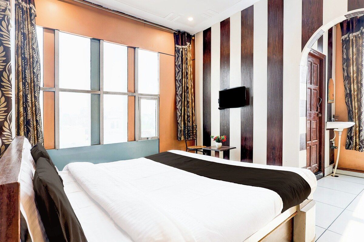 Ein Hotelzimmer mit einem großen Bett, einem flachbildfernseher an der Wand und einem fenster mit Vorhängen.