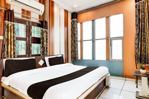 Ein Hotelzimmer mit einem großen Bett, einem Vorhangfenster, einem Nachttisch mit einer Vase und einer Klimaanlage.