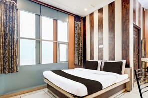 Ein Hotelzimmer mit einem großen Bett, einem Vorhangfenster, einer Holzvertäfelung und einer Tür.